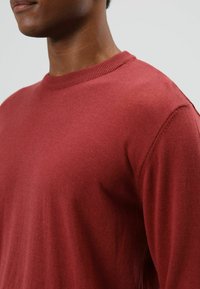 Rode trui met lange mouwen van zacht materiaal, voorzien van een geribde ronde hals en een aangesloten pasvorm, met een gladde textuur en minimale details.