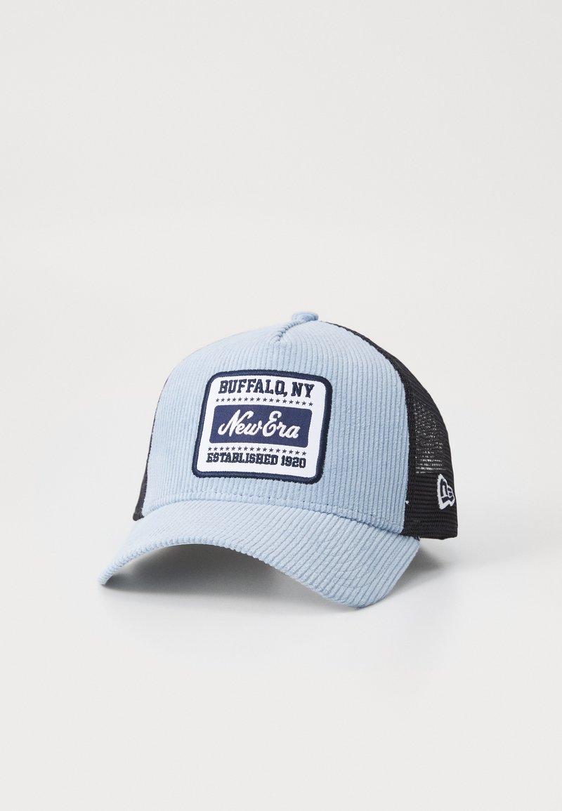 Gorra de pana azul claro con malla negra en la parte trasera, presenta un parche bordado rectangular con texto, estrellas y un logotipo de marca.