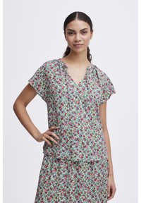 Haut à manches courtes floral en tissu léger avec un col en V et des détails froncés, présentant un motif de fleurs rouges, roses et vertes.