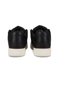 Black leather sneakers with a textured back, contrasting cream sole, and padded collar. Features logo detail on the heel.