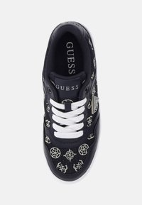 Black sneaker with white laces and rubber sole, featuring embroidered circular designs and a branded tag on the tongue.