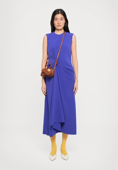 O rochie fără mâneci, de culoare mov, cu detalii pliate, asortată cu o geantă maro tip crossbody, colanți galbeni și tocuri albe ascuțite.