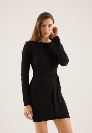 Black knit dress with a fitted silhouette, long patterned sleeves, and a matching belt at the waist. Textured diamond design on sleeves.