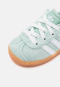 Baskets en suède vert menthe avec des lacets blancs et trois rayures blanches, agrémentées d'une semelle en caoutchouc gomme texturée.