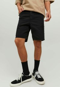 Shorts in denim nero con taglio dritto, dettagli sulle tasche, abbinati a calzini neri e sneakers in bianco e nero. Tessuto liscio e vestibilità casual.