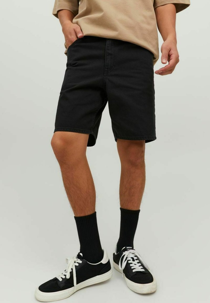 Shorts in denim nero con taglio dritto, dettagli sulle tasche, abbinati a calzini neri e sneakers in bianco e nero. Tessuto liscio e vestibilità casual.