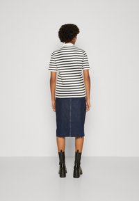 Polo a righe in bianco e nero a maniche corte abbinato a una gonna a tubino in denim scuro e stivaletti neri con tacco chunky.