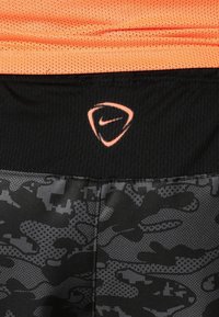 Gros plan sur un vêtement de sport camouflage noir et gris avec une ceinture noire et un logo Nike triangulaire orange sur la ceinture.
