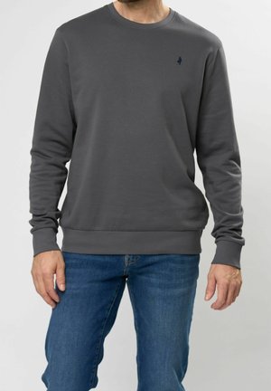 Homme portant un sweat-shirt à manches longues gris foncé uni et un jean bleu, debout, les bras détendus le long du corps.