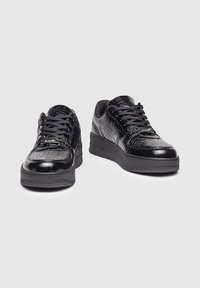 Zapatillas negras hechas de cuero con textura de estampado de cocodrilo, con acentos de cuero suave, cordones negros y una suela de goma gruesa.