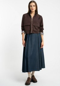 Brązowa krótka kurtka z dwoma przednimi kieszeniami, w zestawie z długą spódnicą z ciemnego dżinsu. Noszona z brązowymi klapkami i beżowymi skarpetami.