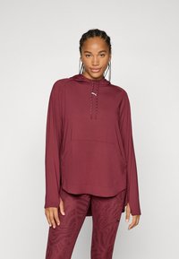 Mörkröd långärmad huvtröja med dragsko i huvan, känguruficka och sidoflikar, ihop med mönstrade mörkröda leggings. Slät, lättviktsmaterial.