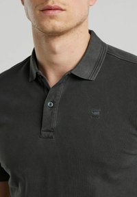 Polo shirt grigio scuro realizzato in tessuto testurizzato, caratterizzato da un colletto classico, pattino con tre bottoni e un piccolo logo sul petto.
