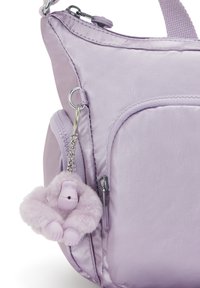 Paarse nylon tas met een gladde textuur, voorzien van een voorvak en een fluffy aap sleutelhanger eraan bevestigd. Rits en hardware in zilver.