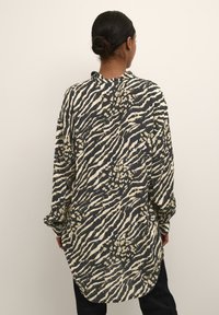 Langærmet skjorte i mørkt stof med et mønster af cremefarvede og brune zebra-striber, med en buet kant og en afslappet pasform.