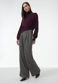 Bordeaux coltrui met losse mouwen, gecombineerd met grijze broek met hoge taille en wijde pijpen, voorzien van een subtiele houndstoothprint.