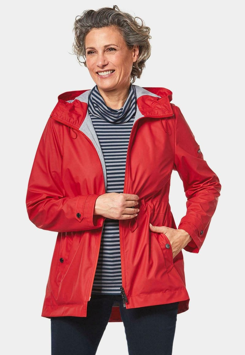 Rote wasserdichte Jacke mit Kordelzug in der Taille, Kapuze und grauem Futter, kombiniert mit einem gestreiften Oberteil. Verfügt über Druckknöpfe und Seitentaschen.