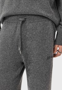 Szare dzianinowe spodnie dresowe z sznurkiem w pasie, teksturowaną tkaniną i haftowanymi detalami w okolicach kieszeni. Wyposażone w ozdobne elementy w kolorze srebrnym.