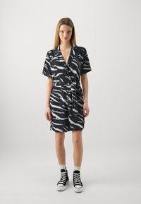 Robe courte à rayures noires et blanches avec col en revers, taille ceinturée et manches courtes, assortie à des baskets montantes noires.