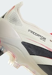 Predator fodboldstøvle med en struktureret off-white overdel, sorte detaljer, røde fine dele og en gennemsigtig hæl med "CONTROL FRAME" etiketten.
