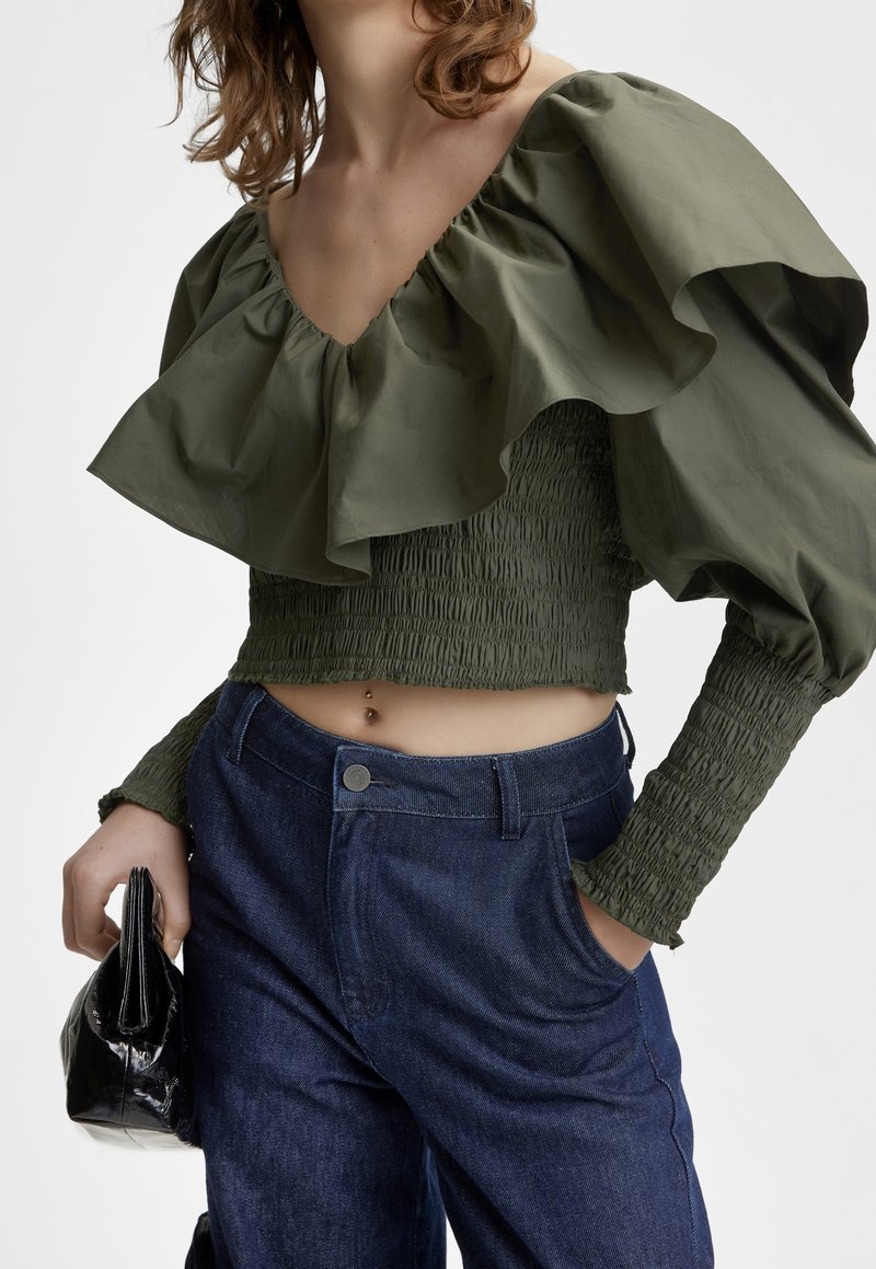 Top corto arricciato verde oliva con design arricciato; abbinato a pantaloni in denim blu scuro a vita alta. Una borsa nera completa il look.