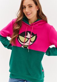 Mikina s kapucí, která má růžovou horní část a zelenou dolní část. Na přední straně má grafiku s kreslenou postavičkou, šňůrky na stažení a žebrovaný lem.