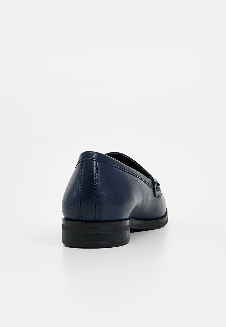 Scarpa slip-on in pelle blu navy con punta arrotondata e tacco in gomma nera basso; texture liscia e design minimale, con dettagli di cucitura sottili.