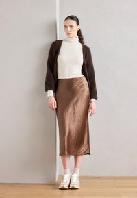 Brauner Satin-Midi-Rock, helles Rollkragensweatshirt, schokoladenfarbener, flauschiger Cardigan und weiße Sneaker. Sanfte Texturen und ein schichtiger Look.