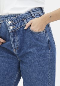 Hoge taille blauwe denim jeans met twee knopen aan de voorkant, vijf-pocket ontwerp en zichtbare stikseldetails. Zachte textuur en klassieke pasvorm.