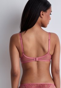 Soutien-gorge en dentelle rose et en mesh avec des fines bretelles, une fermeture à agrafes et des détails décoratifs à l'arrière ; son design sans coutures met en valeur une silhouette lisse.