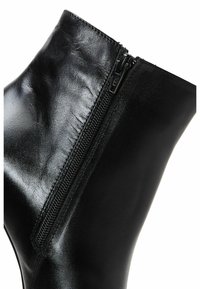 Bottine en cuir noir avec fermeture éclair latérale et texture lisse légèrement brillante.