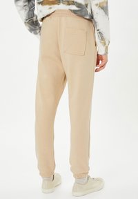 Pantalones jogger beige hechos de tela suave, con una cinturilla elástica, tobillos ajustados y un bolsillo trasero. Diseño minimalista con textura lisa.
