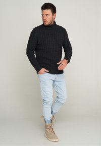 Dunkelgrauer, kabelgestrickter Rollkragenpullover, getragen mit hellblauen Jeans und beigen Schnürboots. Der Pullover hat strukturierte Details im gesamten Design.