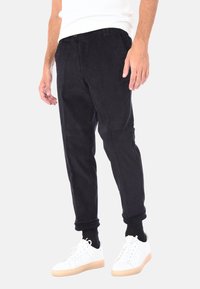 I pantaloni jogger in corduroy neri presentano un design affusolato e polsini elasticizzati, abbinati a sneakers bianche per un contrasto.