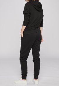 Svart bomullshuvtröja med känguruficka, justerbar dragsko på huven, ribbade ärmslut och matchande svarta joggingbyxor. Vita sneakers fulländar looken.