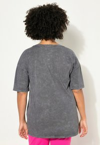 Graues, übergroßes T-Shirt mit kurzen Ärmeln, strukturierter Oberfläche und Rundhalsausschnitt. Nahtdetails sind entlang des Saums und der Schultern sichtbar.