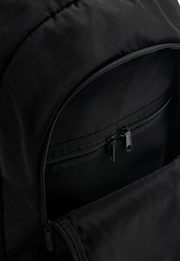 Fekete hátizsák tágas fő rekesszel, cipzáras elülső zsebbel, ami hálós béléssel rendelkezik, és sima szövettextúrával.