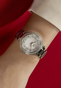 Orologio da polso in tono argento con quadrante bianco decorato, numeri romani, bezel testurizzato e bracciale metallico bicolore.