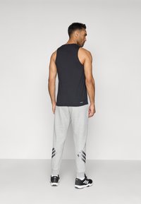 Svart ärmlös t-shirt och grå joggingbyxor med svart och vitaccent. Modell sedd bakifrån, bärande svarta träningsskor.