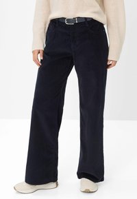 Navy corduroy wide-leg pants with front pockets, zip and button closure, and a matching belt. Light-colored sneakers complete the look.