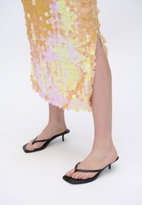 Paillettenkleed met iriserende gele en roze ronde pailletten, splitnaaddetail, gecombineerd met zwarte hoge teenslippers.