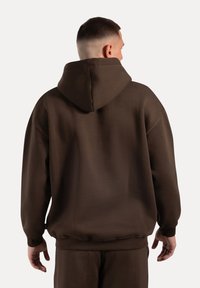 Brauner Hoodie mit großzügigem Design, ausgestattet mit einer großen Kapuze, gerippten Bündchen und Saum, gefertigt aus einem glatten, dicken Stoff.