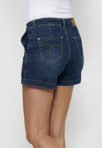 Temno modri jeans kratke hlače z oprijetim krojem, ki imajo zadnji žep z edinstvenim dekorativnim šivom in standardnim robom.