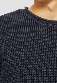 Dunkelblau gestrickter Pullover mit strukturiertem Muster, Rundhalsausschnitt und geripptem Kragen. Der Stoff wirkt weich mit einer leicht lockeren Webart.