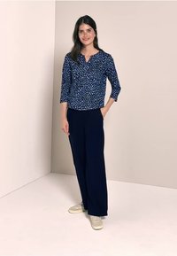 Blusa azul marino con un patrón blanco texturizado, mangas tres cuartos, combinada con pantalones anchos azul marino y zapatillas de color claro.