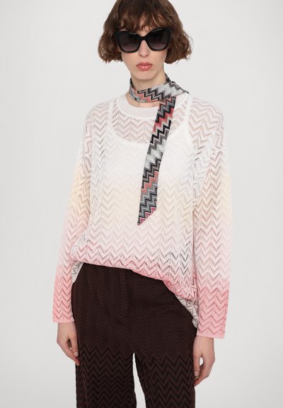 Pulover ușor, tricotat, cu un model în zigzag în nuanțe gradient de la alb la roz, purtat cu o eșarfă cu model și pantaloni negri, texturati.