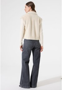 Crèmekleurige fleecejack met een kraag, gecombineerd met donkergrijze wijde jeans. Zichtbare stitches en zijzakken op de jeans.