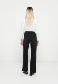 Black wide-leg jeans with a high waist, paired with a long-sleeve white shirt. The outfit features minimalistic design and a sleek silhouette.