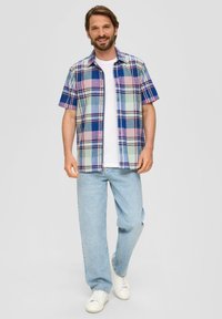 Camicia a maniche corte a quadri nei toni del blu, verde e rosa. Presenta una chiusura frontale con bottoni e una vestibilità comoda. Abbinata a jeans azzurri e sneakers bianche.