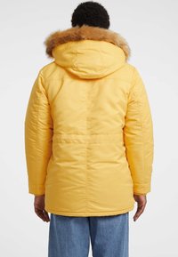 Geel gewatteerde parka-jack met een bontvoering in de capuchon, met een getailleerde taille, lange mouwen en een gladde textuur.